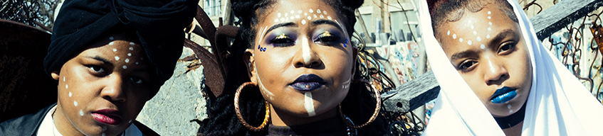Close-up of three afrofuture youth organizers with serious expressions, wearing makeup and facepaint on their cheeks and foreheads