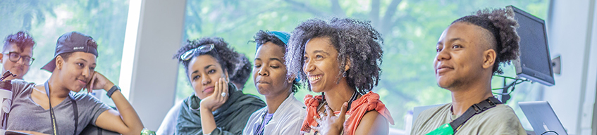 A row of 5 people seated in an AMC session, smiling, with trees out the windows in the background