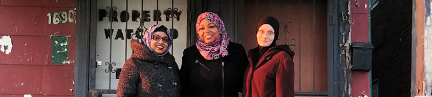MuslimARC members standing on a porch in front of a door with the words "property watched" painted on it.