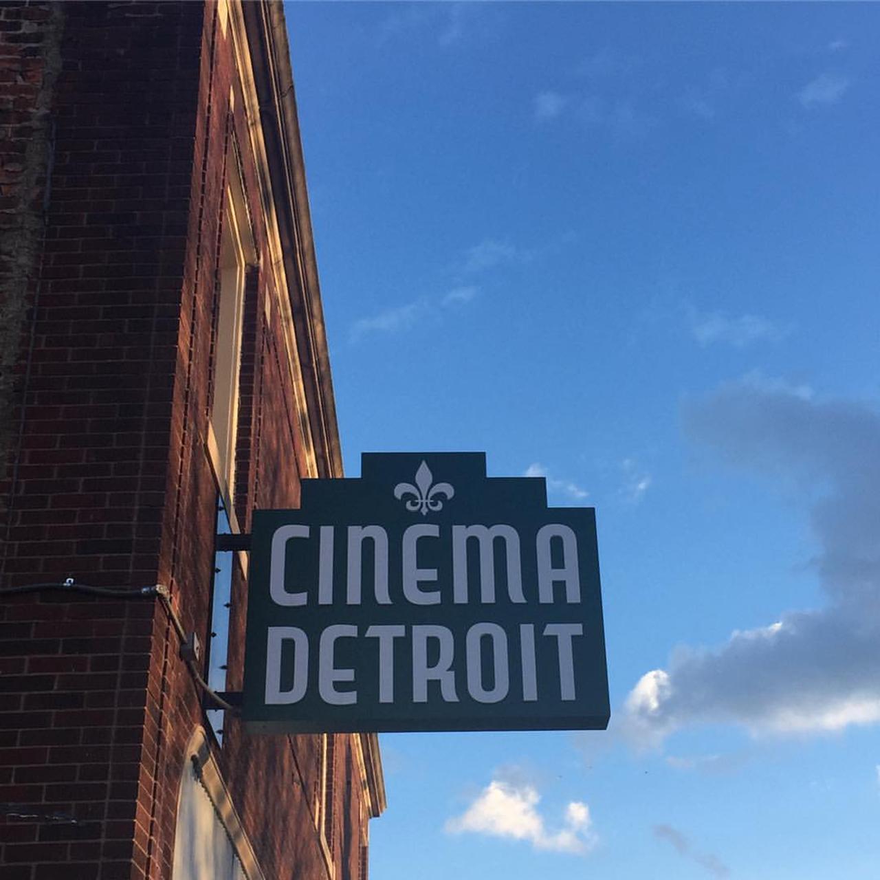 Cinema Detroit sign - green sign with white lettering - on a brick building against the blue sky