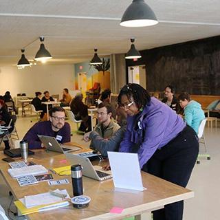 Image of a data discotech. A room full of tables surrounded by people learning about various technology topics.