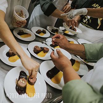 A table full of plates of the same food, with many hands reaching in adding food to the plates