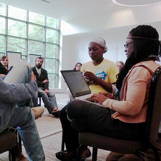 Two people on laptops in the forefront, sitting in a circle of people