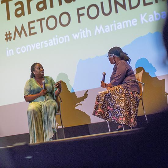 Tarana Burke and Mariame Kabe sitting in chairs on a stage, their names projected onto a screen behind them